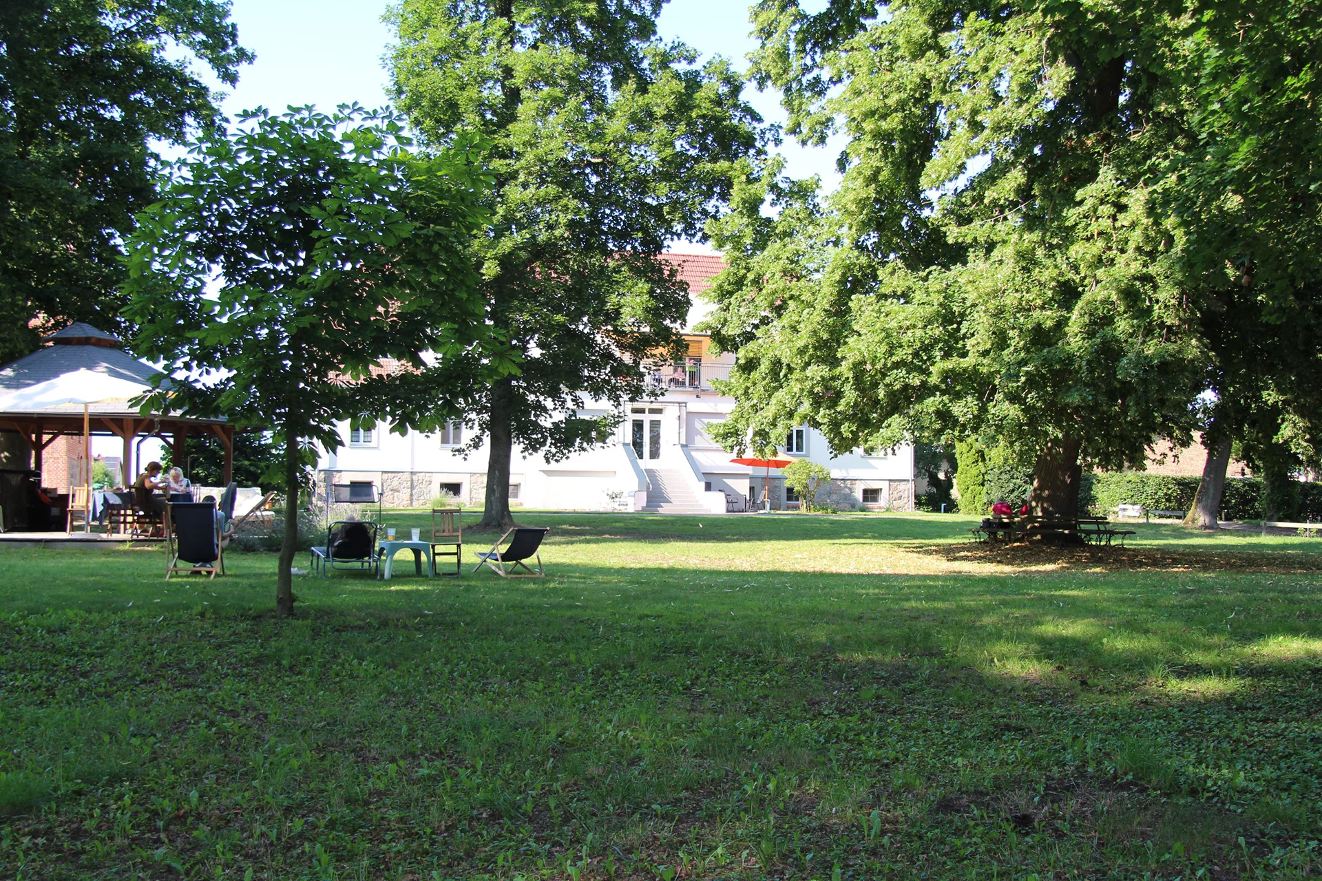 Blick auf das Gutshaus Seehausen mit großer Wiese und schattigen Bäumen